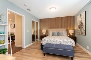 Une chambre à coucher avec un lit, des lampes de chevet, un mur recouvert de lambris en bois, un banc bleu et une porte donnant sur une autre pièce.