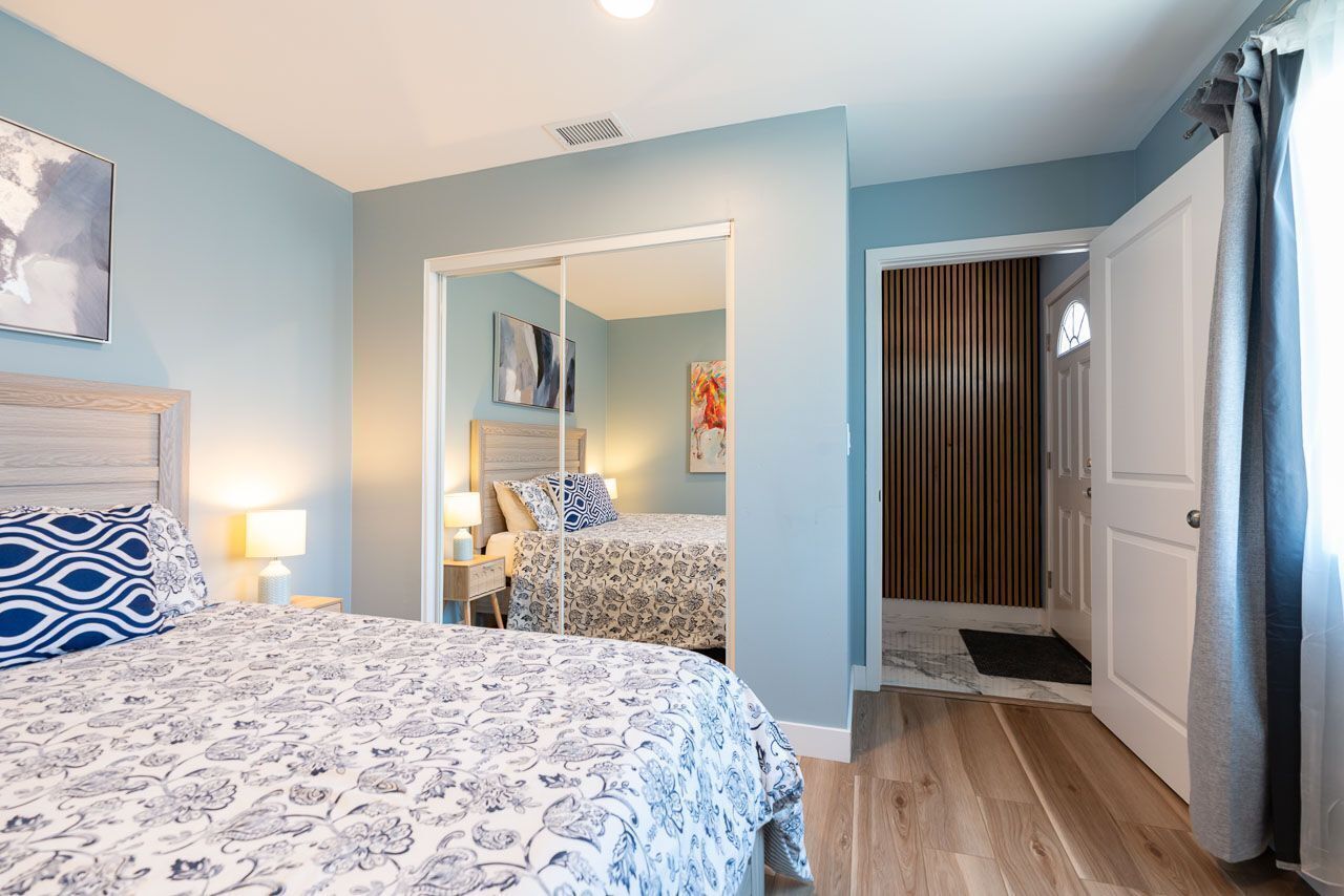 A bedroom with a bed, bedside tables, and a mirror. There is a door leading to another room.