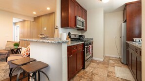 Cocina equipada con microondas, estufa y refrigerador. Cuenta con una barra con taburetes y un rincón de descanso con sofá y mesa de centro.
