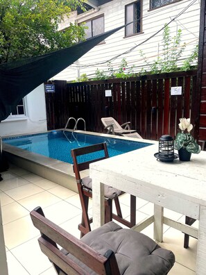 A backyard with a swimming pool, a wooden deck, a table with chairs, and a potted plant.