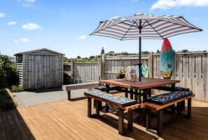 Un terrazzo in legno con tavolo da picnic e panchine, un ombrellone a righe e una tavola da surf.