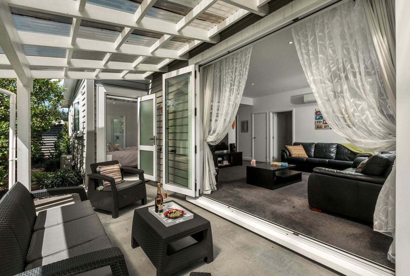Ein modernes Wohnzimmer mit Glaswand, einer schwarzen Ledersofa und einem Essbereich mit Tisch und Stühlen.