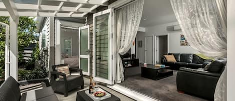 A modern living room with a glass wall, a black leather sofa, and a dining area with a table and chairs.