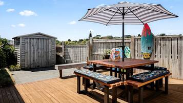 A wooden deck with a picnic table and benches, a striped umbrella, and a surfboard.