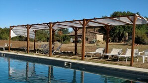 Kirkasvetinen uima-allas, jonka ympärillä on aurinkotuoleja ja jonka yläpuolella on pergola.