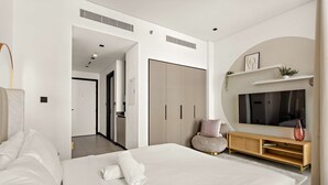 A modern hotel room with a large bed, a TV, a wooden console, and a hallway leading to another room. - Luxury Studio in Business Bay With Pool and gym (Dubai)
