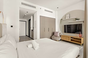 Ein modernes Hotelzimmer mit einem großen Bett, einem Fernseher, einer Holzkonsole und einem Flur, der in ein weiteres Zimmer führt.