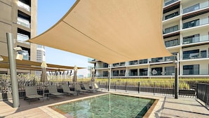 A rooftop pool with lounge chairs and a canopy, surrounded by a modern building with balconies. - Luxury Studio in Business Bay With Pool and gym (Dubai)