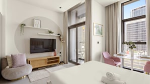 A modern hotel room with a large bed, a TV, a seating area with a chair, and a balcony with a table and chairs. - Luxury Studio in Business Bay With Pool and gym (Dubai)