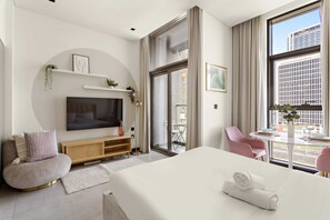 Ein modernes Hotelzimmer mit einem großen Bett, einem Fernseher, einer Sitzecke mit einem Sessel und einem Balkon mit Tisch und Stühlen.