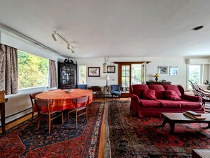 A living room with a round table, red sofa, and patterned rugs. - Spacious Waterfront Cottage with Private Beach and Deck, Near Acadia National Park in Hancock Point, Maine (Hancock)