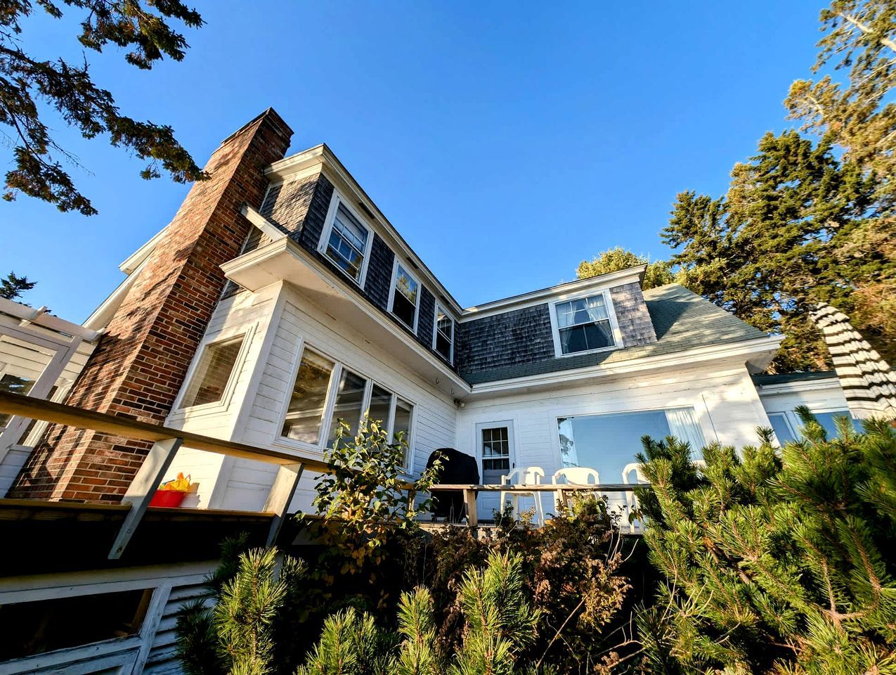 A two-story house with a brick chimney, white siding, and a deck with outdoor furniture.
