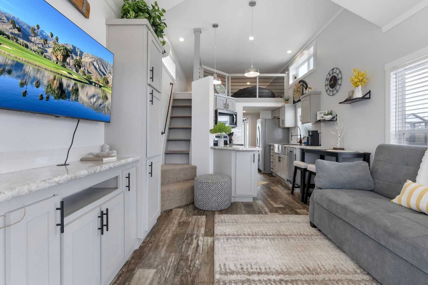 A modern kitchen with white cabinets, a central island, and a dining area with a grey sofa.