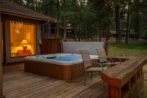 A hot tub on a wooden deck with chairs, a table, and a room with a lamp. - Relax with Mountain and BBR Golf Course Views (Sisters)