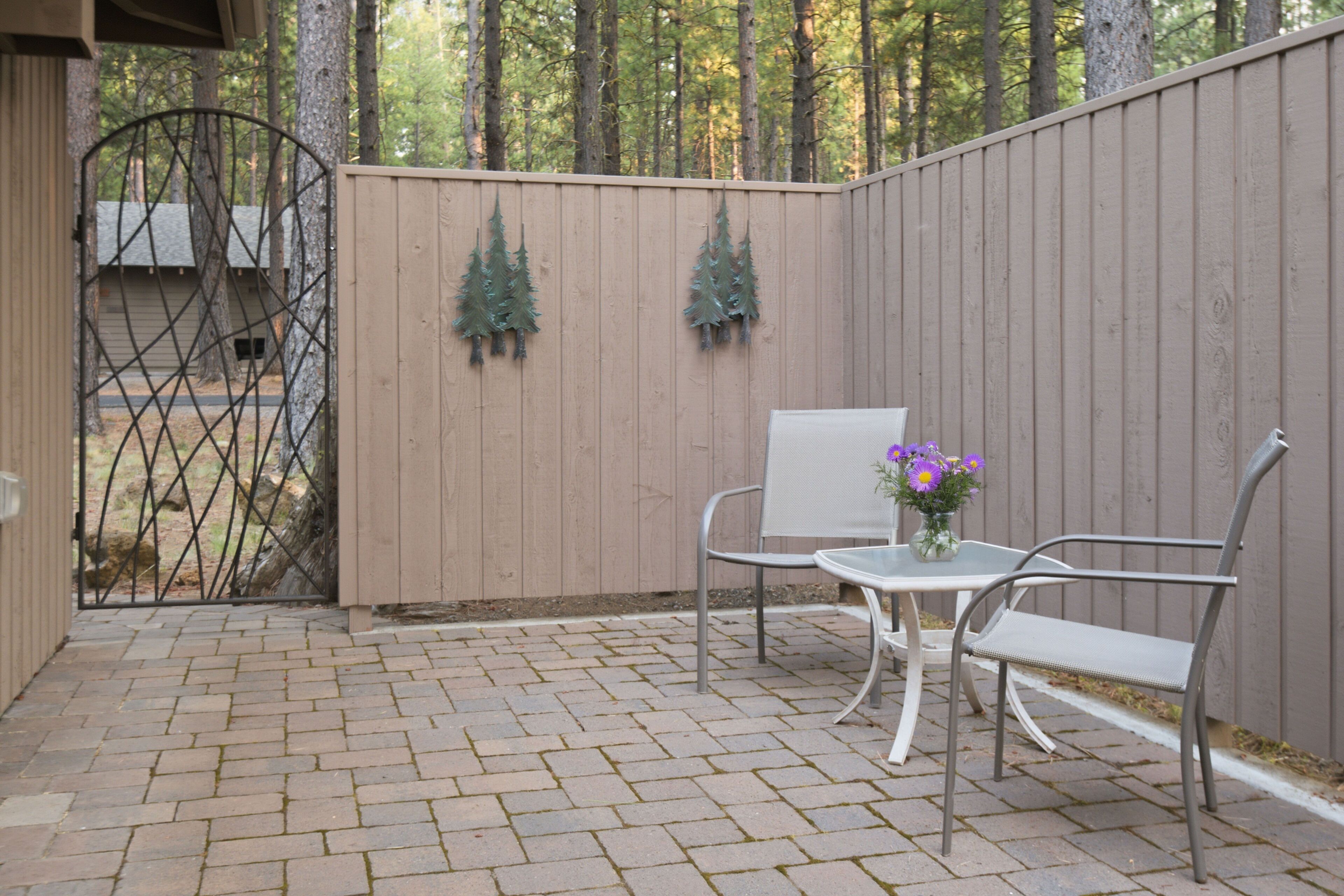 A patio with a metal gate, two chairs, a table, and a vase with flowers.