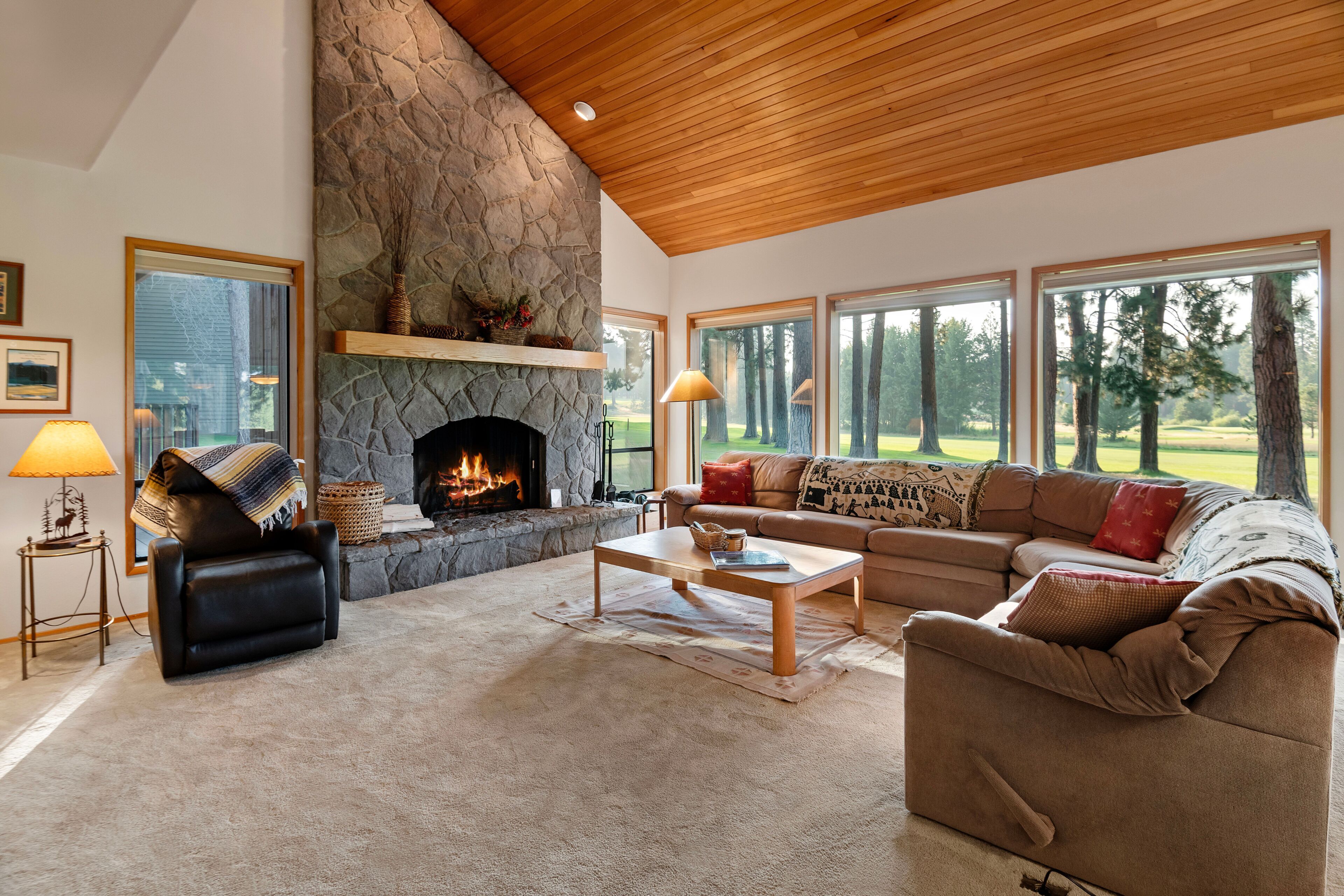 A spacious living room with a stone fireplace, leather furniture, and large windows offering a view of a golf course.