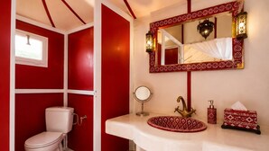 A bathroom with a red and white color scheme, a white sink with a patterned basin, a round mirror, a toilet, and a decorative wall mirror. - Moon Luxury Camp  (Merzouga)