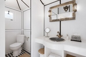 A bathroom with a toilet, sink, mirror, and decorative wall piece.