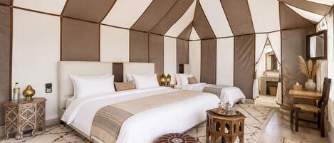 Quarto com tenda, uma cama grande, mesas de cabeceira, um banquinho pequeno e um tapete.