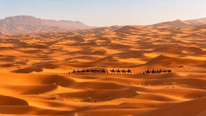 A desert landscape with sand dunes and a group of people riding camels.