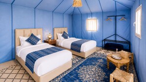 A room with two beds, a hanging light fixture, a small table with a bottle, and a hanging rack.