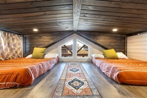 Ein Schlafzimmer mit zwei Betten, einer Holzbalkendecke, einem großen Fenster und einem gemusterten Teppich.