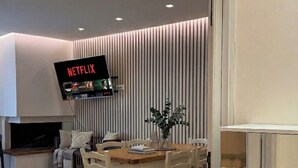 Uma sala de estar moderna com uma mesa de jantar de madeira, cadeiras e uma TV de tela plana na parede exibindo o logotipo da Netflix.