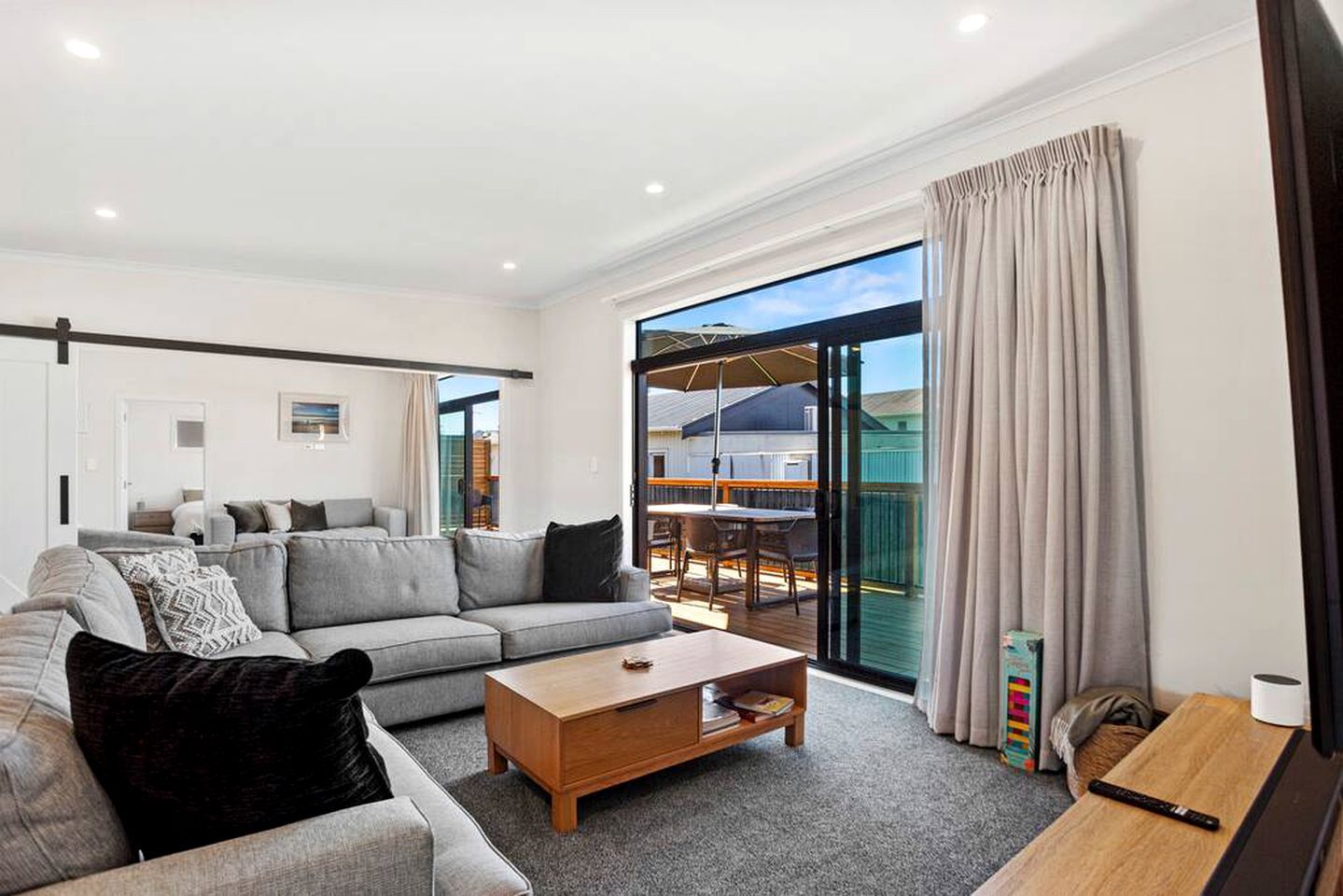 A modern living room with a grey sectional sofa, a wooden coffee table, and a sliding glass door leading to an outdoor patio.