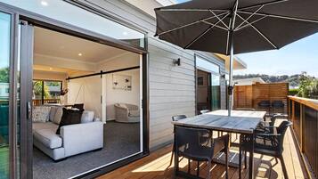 Eine moderne Terrassenanlage mit Tisch und Stühlen, einem großen Sonnenschirm und einer Glasschiebetür zu einem Innenwohnraum.