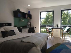 Ein modernes Schlafzimmer mit Bett, Schreibtisch, Stuhl und großen Fenstern.