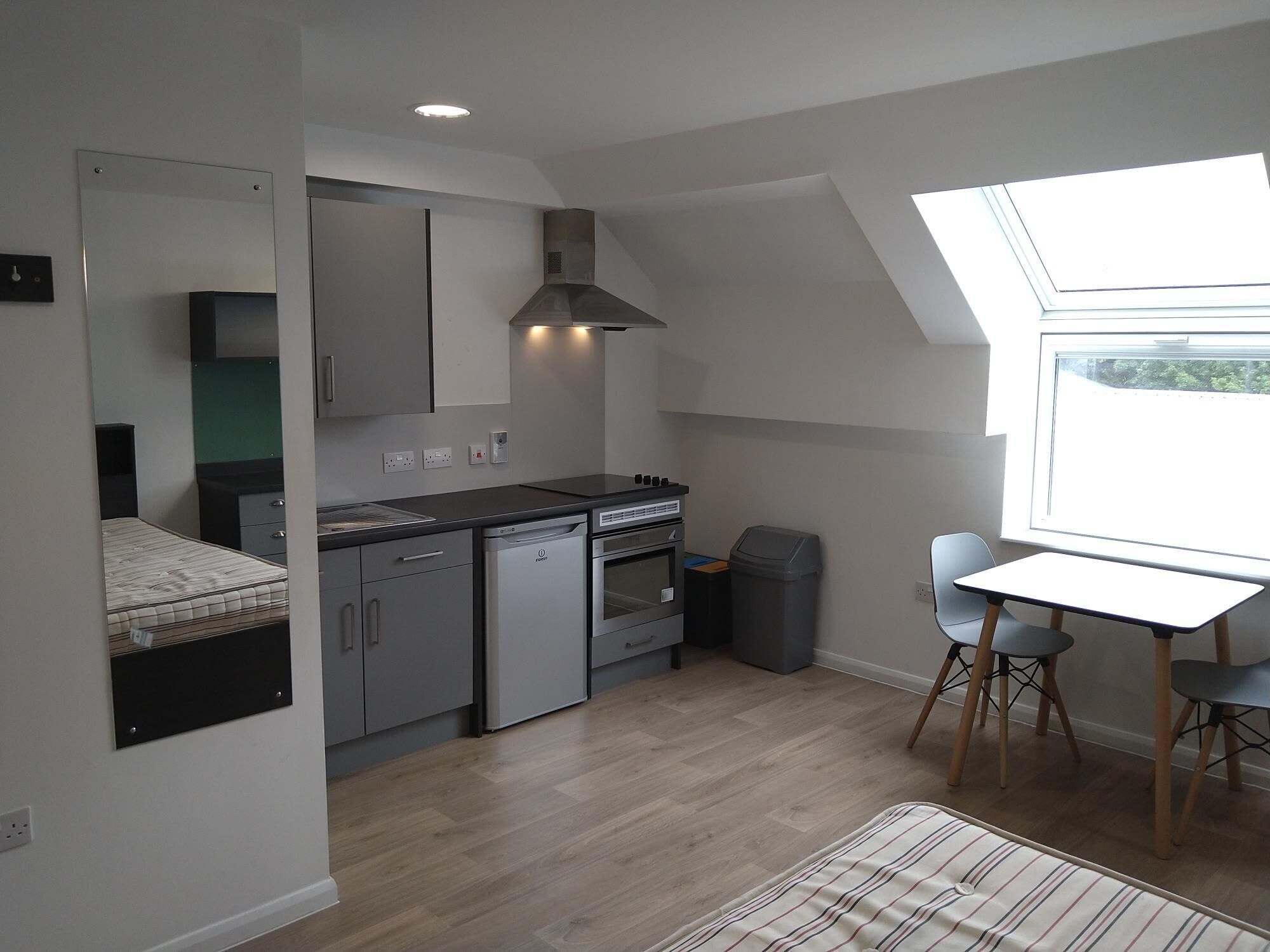 A compact kitchen with a built-in oven, a dishwasher, and a stove. There's a small trash bin and a window providing natural light.