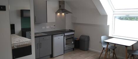 A compact kitchen with a built-in oven, a dishwasher, and a stove. There's a small trash bin and a window providing natural light.