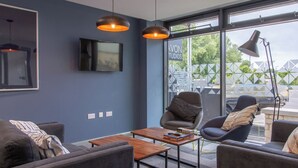 A modern living room with a flat-screen TV, two armchairs, a coffee table, and pendant lights. - Avon Studios Bath (Bath)