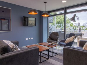 A modern living room with a flat-screen TV, two armchairs, a coffee table, and pendant lights. - Avon Studios Bath (Bath)