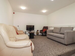 A living room with a leather recliner, a grey sofa, a television, and a small table with decorative items. - Newseal House (St Austell)
