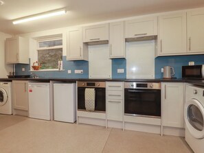 A compact kitchen with white cabinets, a built-in oven, a microwave, and a washing machine. - Newseal House (St Austell)