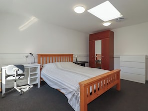 A bedroom with a bed, desk, chair, wardrobe, and a skylight. - Newseal House (St Austell)