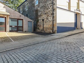 A stone building with a ground-floor entrance, a small porch, and a paved street. - Newseal House (St Austell)