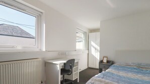Une chambre à coucher comprenant un lit, un bureau, une chaise, une armoire et un radiateur.