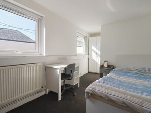 A bedroom with a bed, a desk, a chair, a wardrobe, and a radiator. - Newseal House (St Austell)