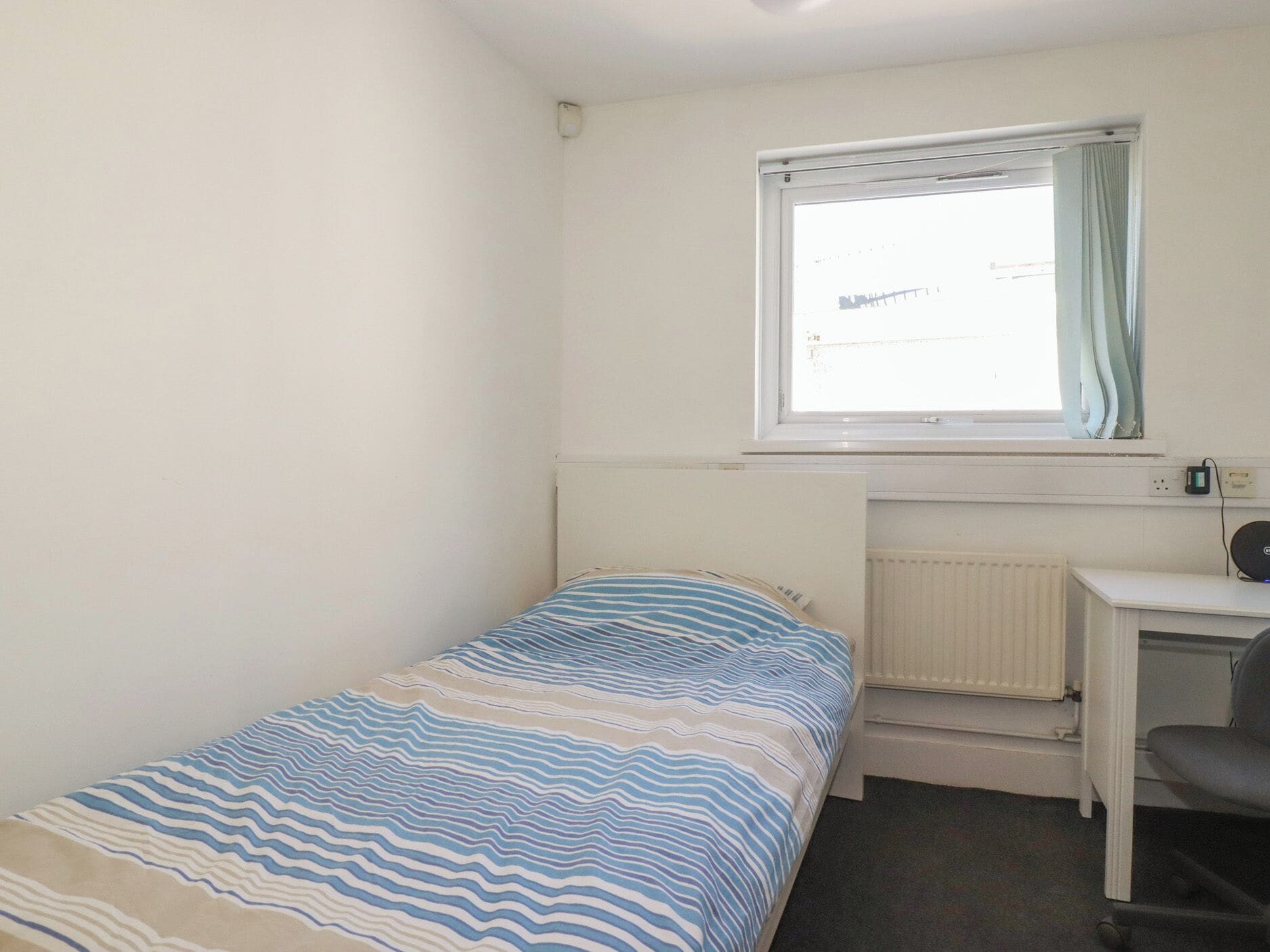 A small, single-bed room with a window, a desk, and a chair.