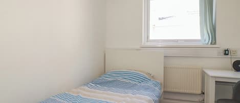A small, single-bed room with a window, a desk, and a chair.