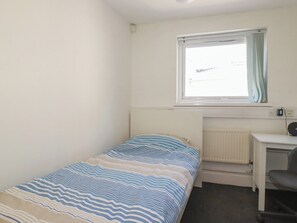 A small, single-bed room with a window, a desk, and a chair. - Newseal House (St Austell)