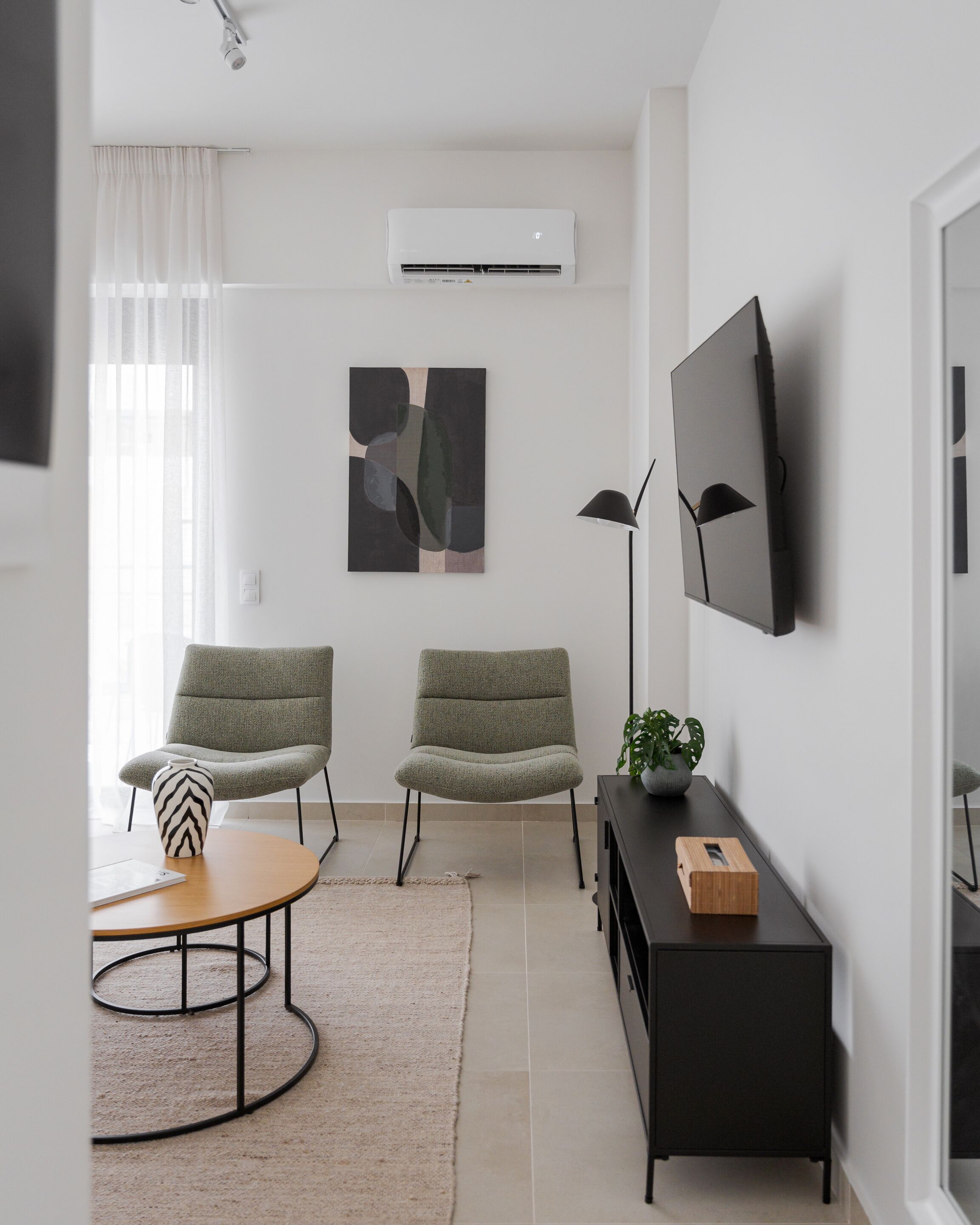 A modern living room with two green armchairs, a round coffee table, a black TV stand, and a mounted flat-screen TV.