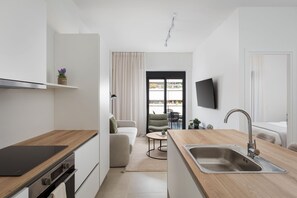 A modern kitchen with a wooden countertop, a built-in oven, a sink, and a dining area with a table and chairs. - Solis Luxury Residences (Glifada)