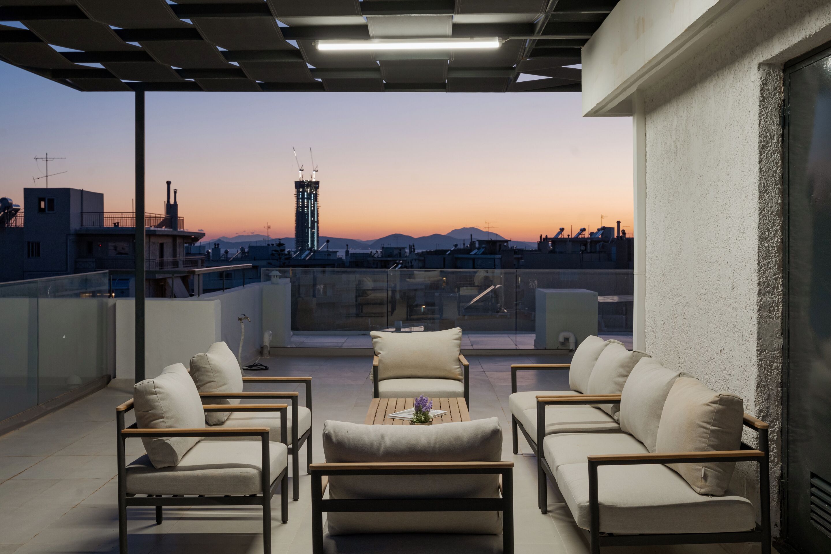 A rooftop terrace with a view of a city skyline at dusk, featuring a seating area with sofas and a coffee table.