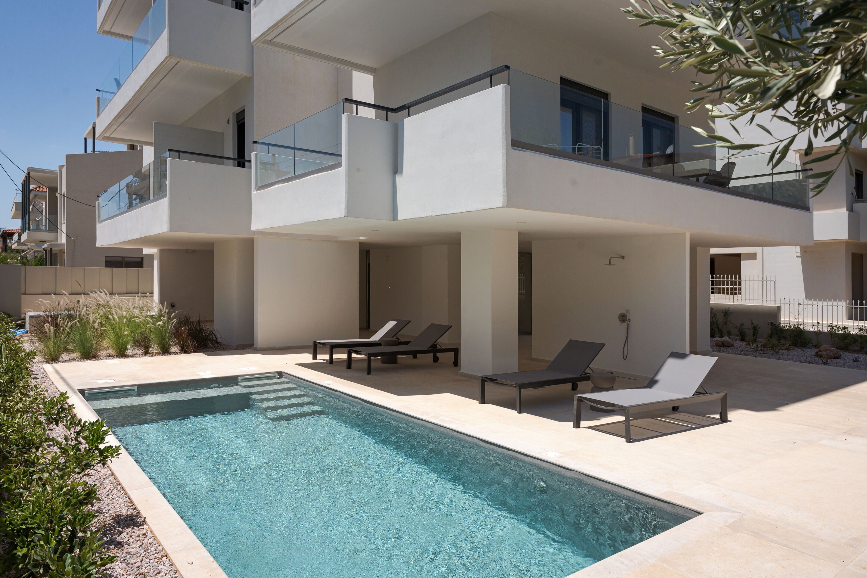 A modern multi-story building with a swimming pool, lounge chairs, and a clear view of the sky.