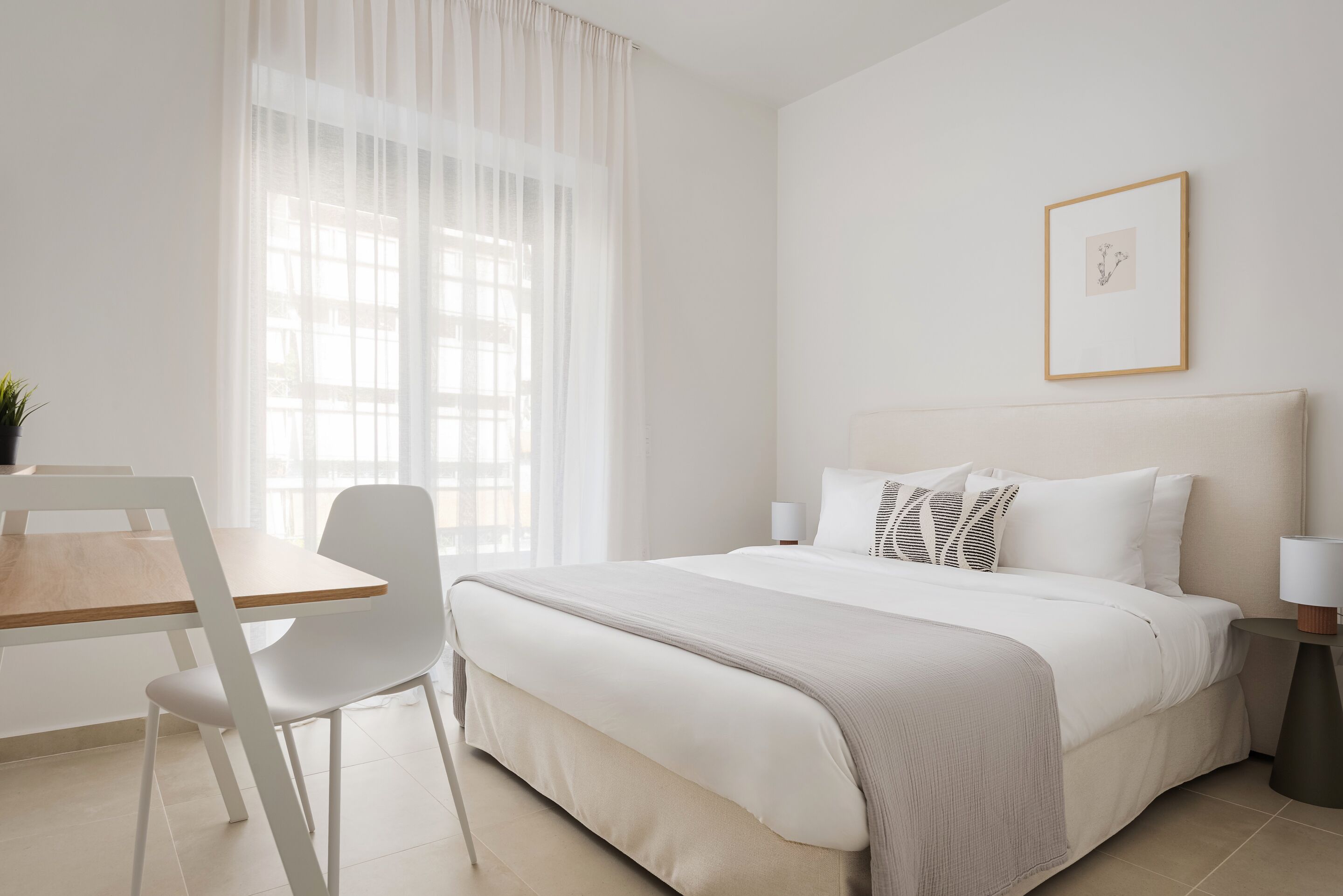 Une chambre d’hôtel avec un lit, une chaise, un bureau et une fenêtre avec des rideaux.