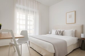 Habitación de hotel con cama, una silla, escritorio y ventana con cortinas.