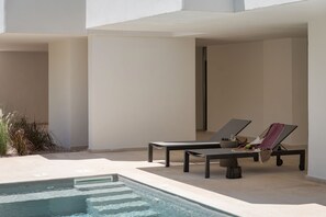 Un área junto a la piscina con dos sillas de descanso, una mesita y una fuente.